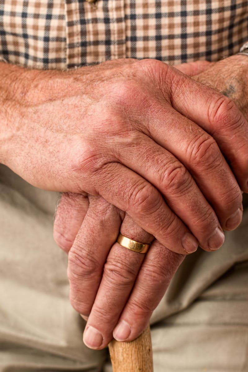 A detailed image of elderly hands clasping a wooden cane, symbolizing aging and support.