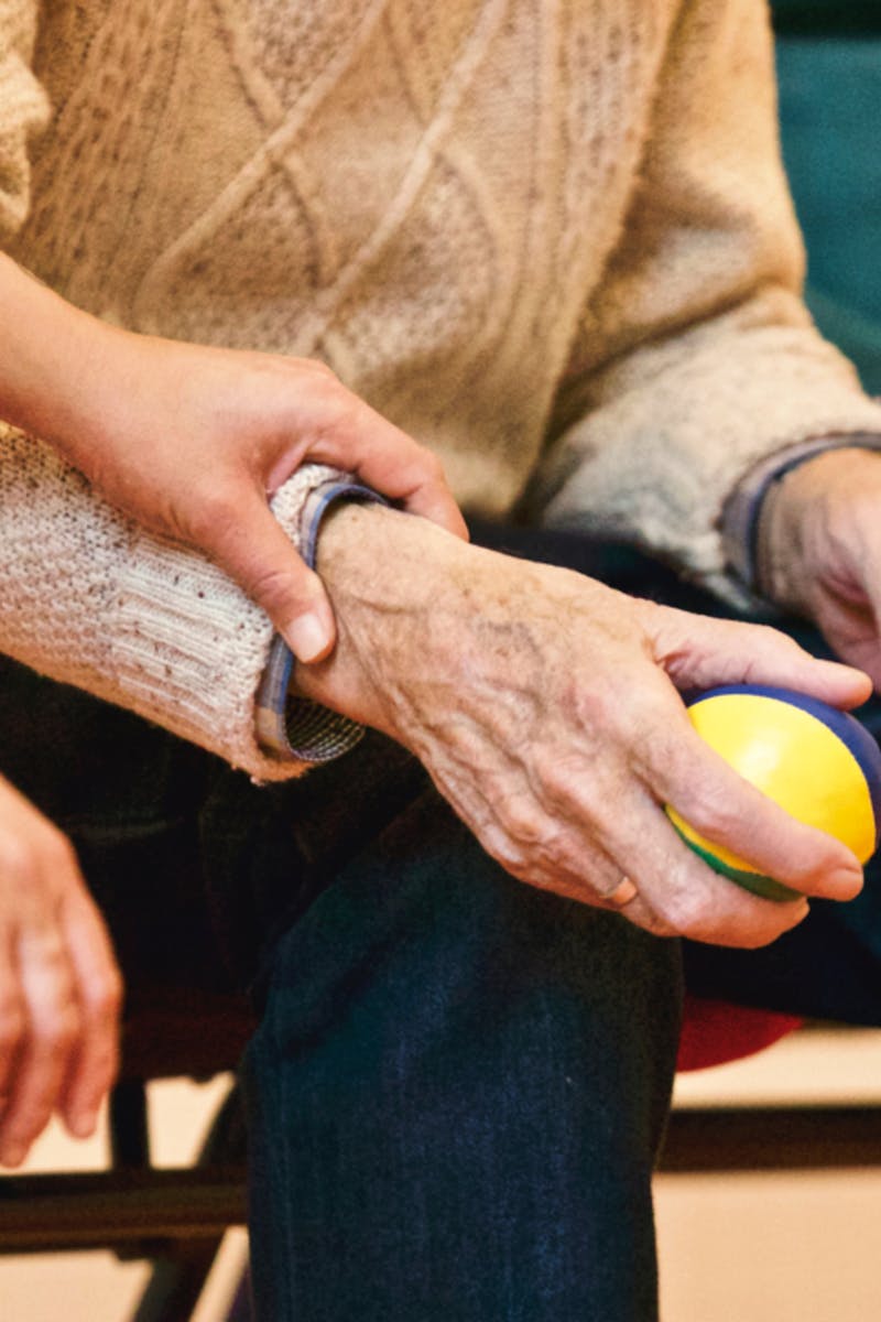 An elderly person receives support from a caregiver, holding hands indoors, showcasing compassion.