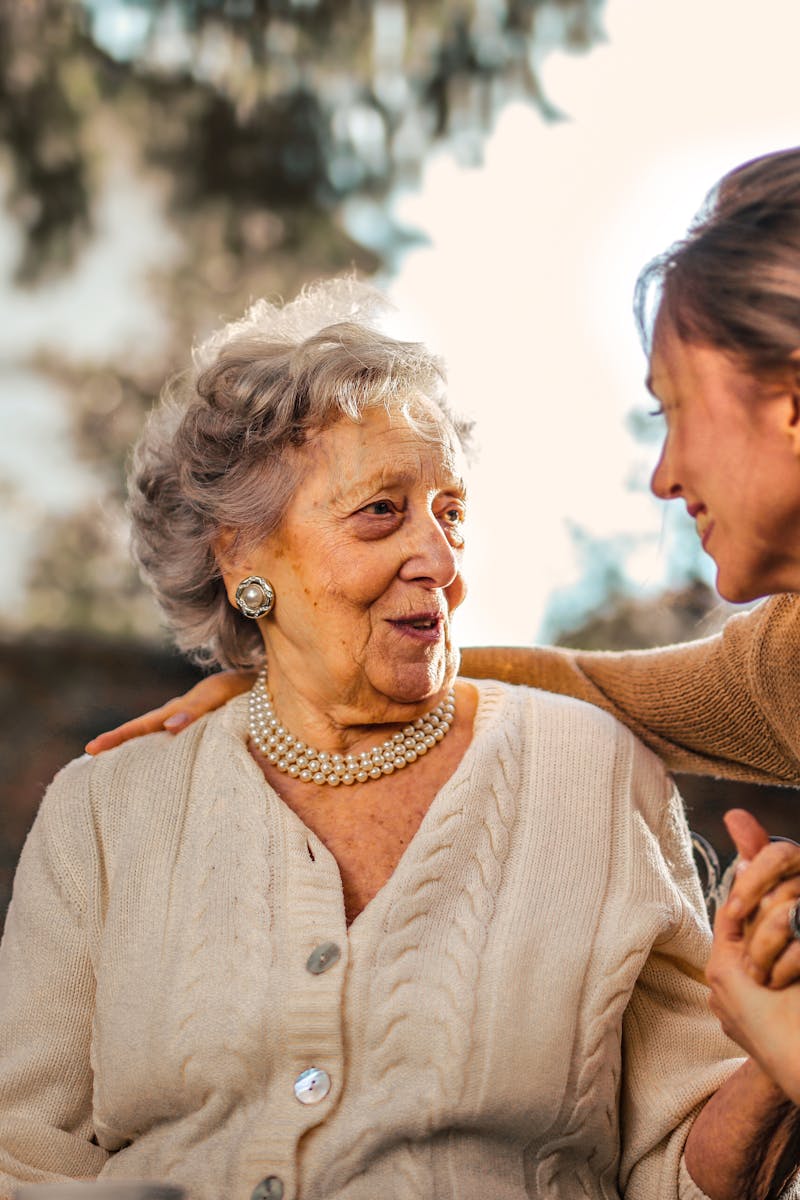 Elderly woman and adult daughter share a joyful, affectionate moment in a sunny garden.