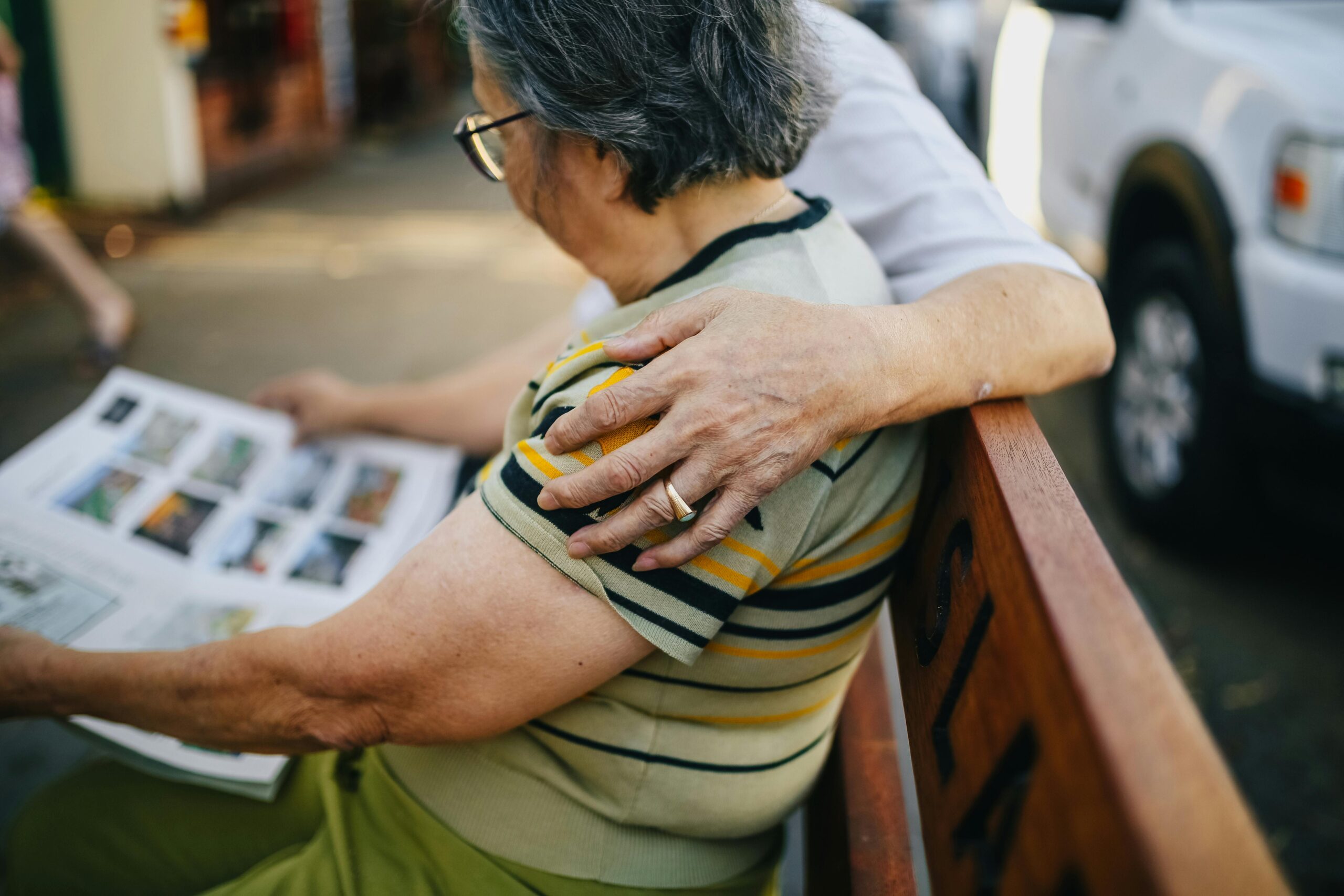 Heartwarming moment with elderly couple reading together while sitting on a bench outdoors.